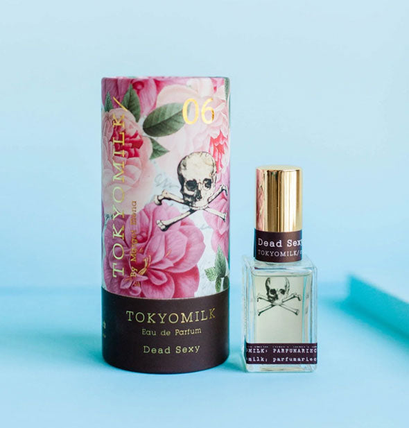 Small square glass bottle of TokyoMilk Dead Sexy Eau de Parfum next to cylindrical pink floral print box, both accented with skull and crossbones graphic
