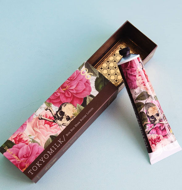 Tube and opened box of TokyoMilk Bon Bon Shea Butter Lotion with pink floral motif and skull and crossbones graphics; box interior features a geometric metallic gold foil pattern