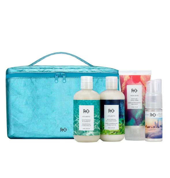 Bottles of R+Co Atlantis Moisturizing B5 Shampoo and Conditioner, High Dive Moisture + Shine Creme, and Skyline Dry Shampoo Powder with metallic blue carrying case