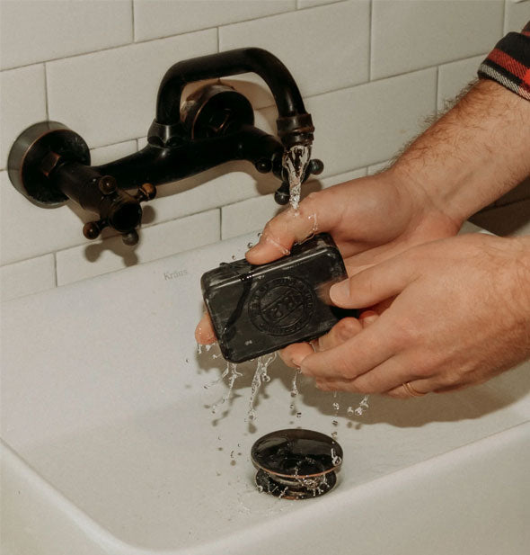 Model wets a black Detox Bar of soap under a running faucet