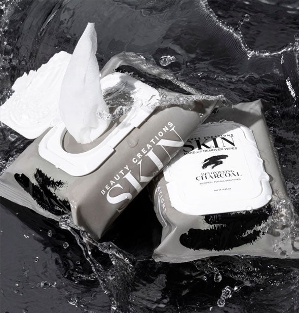 One closed and one opened pack of Detoxifying Charcoal Beauty Creations Skin Makeup Remover Wipes staged in splashing water on a dark backdrop