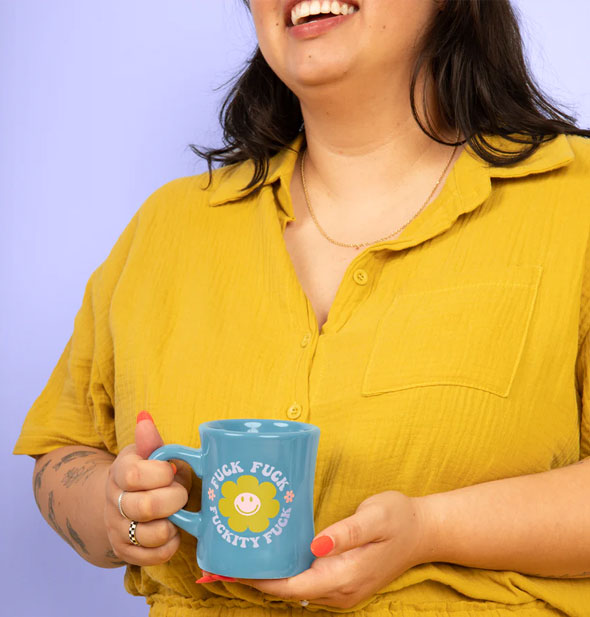 Smiling model in a mustard yellow shirt holds the blue Fuck Fuck Fuckity Fuck diner mug in both hands