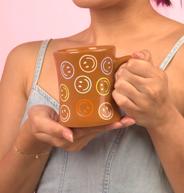 Model holds a brown smiley face diner mug in both hands