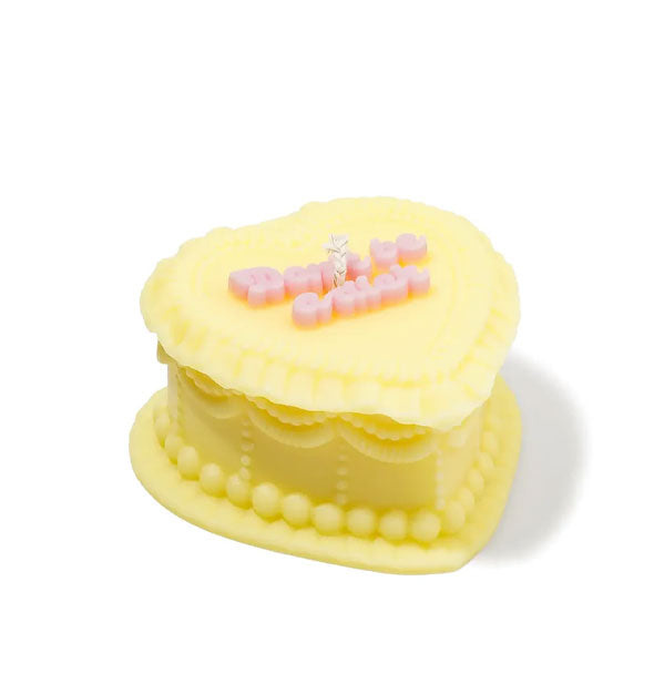 Yellow heart-shaped candle designed to resemble an ornately frosted cake with the words, "Don't be a dick" on top in pink script lettering