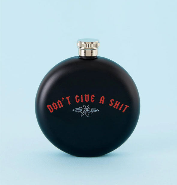 Round black flask says, "Don't Give a Shit" in red Gothic-style font with light daisy illustration below it