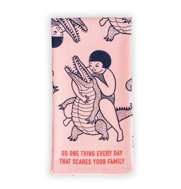 Pink dish towel with illustration of girl wrestling a crocodile says, "Do one thing every day that scares your family"