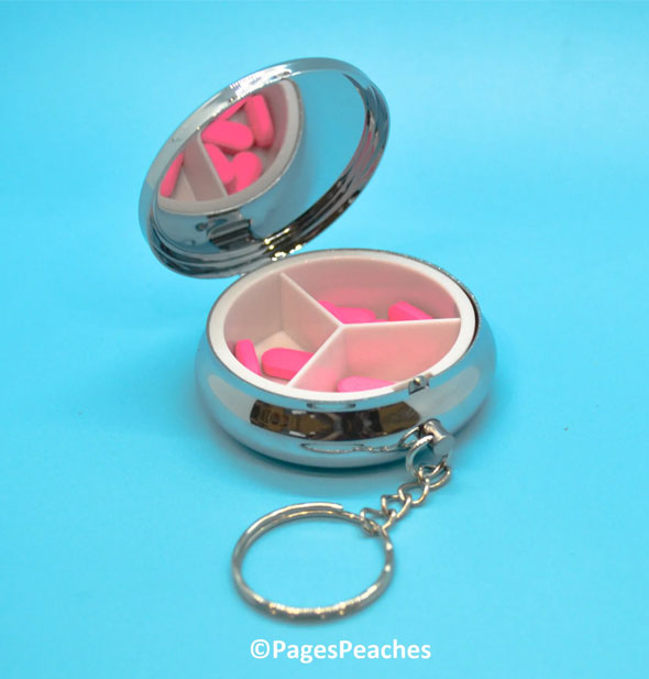 Opened round silver pill case keychain reveals 3-compartment divider inside holding several pink tablets
