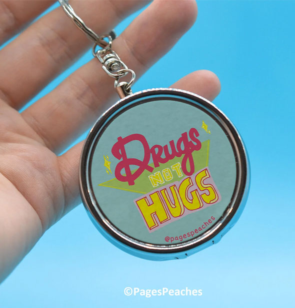 Model's hand holds a Drugs Not Hugs pill case keychain by the ring