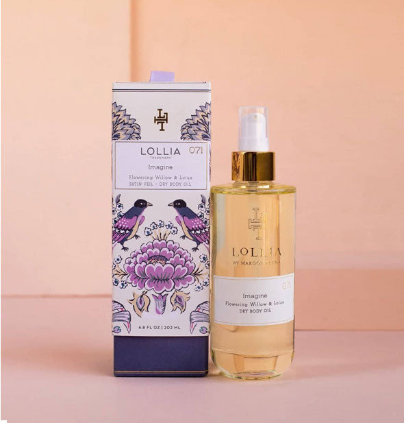 Glass bottle of Lollia Imagine Flowering Willow & Lotus Dry Body Oil sits next to a decorative box with blue and purple floral and birds design