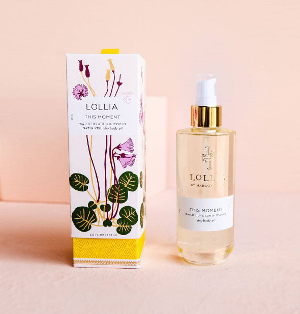 Clear glass bottle of Lollia This Moment Waterlily & Sun Blossoms Dry Body Oil next to decorative floral box