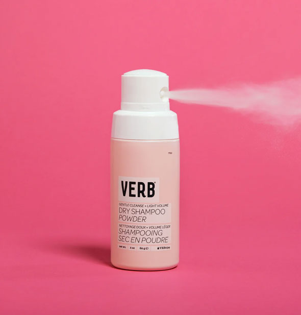 A fine mist of product is dispensed from a bottle of Verb Dry Shampoo Powder against a dark pink backdrop