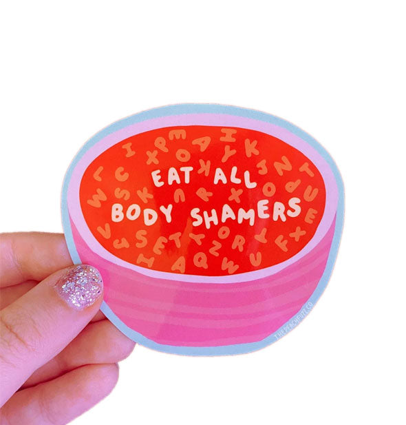 Model's hand holds a sticker designed to look like a pink bowl of red alphabet soup with the message, "Eat all body shamers" most prominent