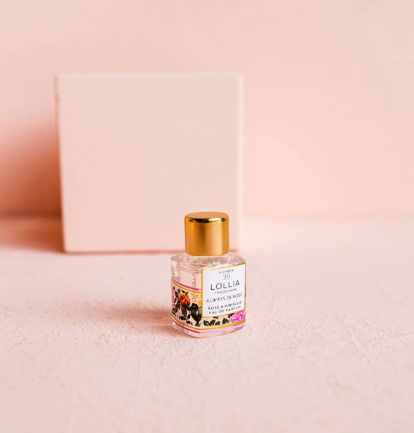 Mini glass Lollia Always In Rose Eau de Parfum bottle with floral design and glass lid set against a pink backdrop
