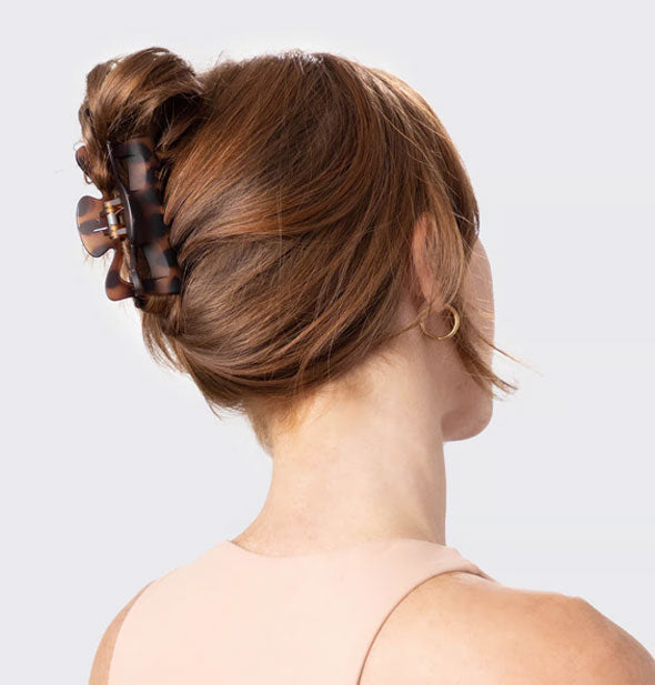 Model wears a matte brown tortoise claw clip in a swept-back, twisted-up hairstyle