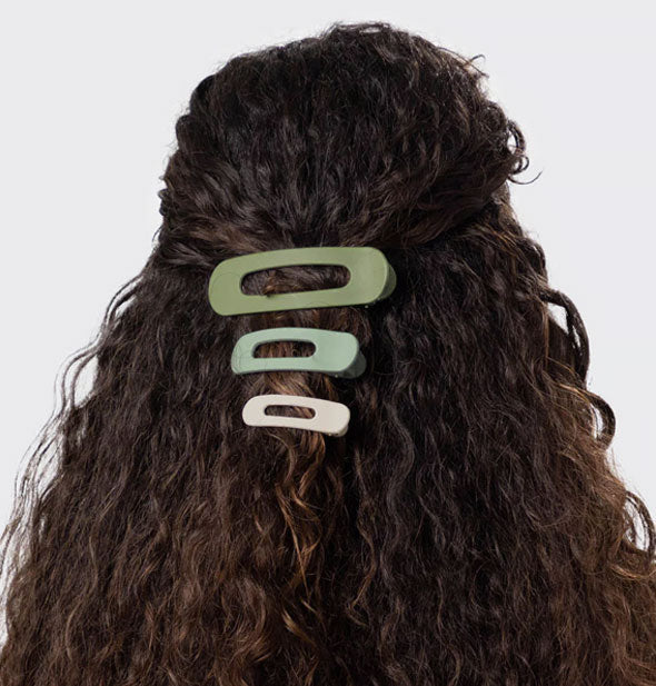 Model wears a series of three green and neutral open-shape ovoid clips in a partially swept-back hairstyle