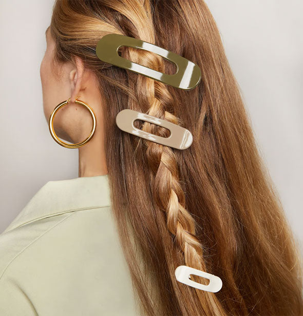Model wears three shiny ovoid hair clips in a neutral color palette in a long braid