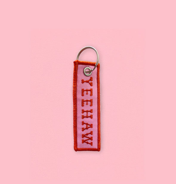 Rectangular pink embroidered keychain tab with red border says, "Yeehaw" in Old West-style lettering