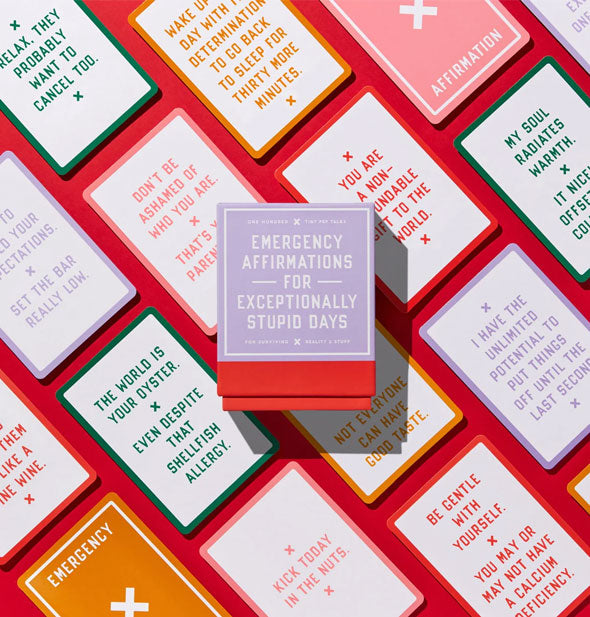 Box of Emergency Affirmations rests on top of cards from the deck on a red surface