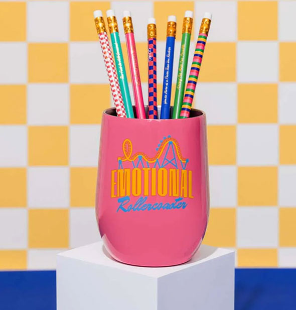 Emotional Rollercoaster wine tumbler is staged on a white cube and filled with colorful pencils against a blue, yellow, and white backdrop