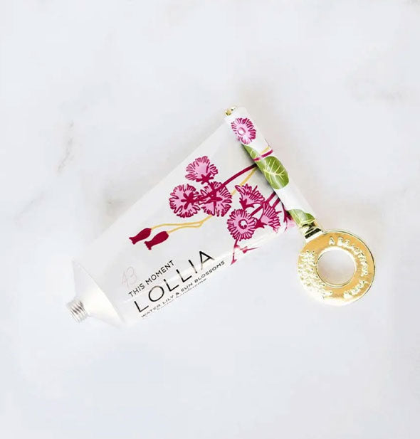 The end of a tube of This Moment Lollia handcreme is partially wrapped around a decorative gold key