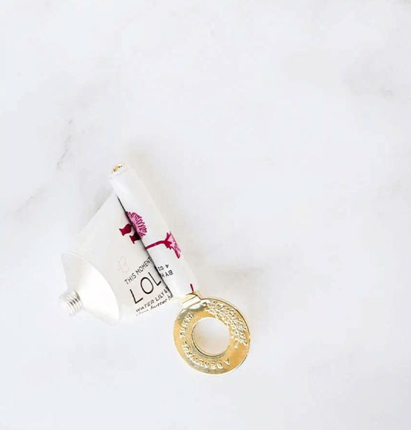 A tube of This Moment Lollia handcreme is mostly wrapped around a decorative gold key