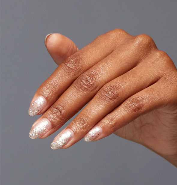 Model's hand wears a light glitter shade of nail polish with an iridescent finish