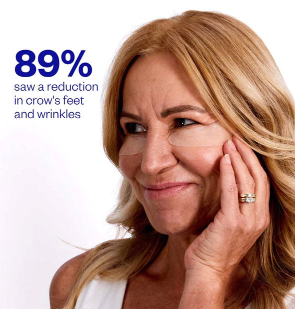 Smiling model wearing a pair of silicone under-eye patches looks toward a label that reads, "89% saw a reduction in crow's feet and wrinkles"