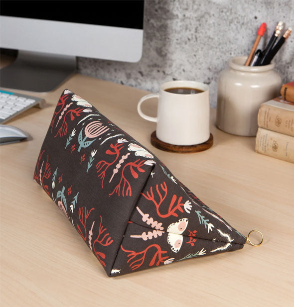 A Far and Away Large Cosmetic Bag lays on its side on a desktop to show its flat bottom and triangular shape