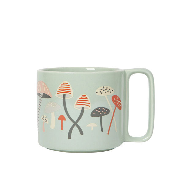 Light green coffee mug with rectangular handle features illustrations of mushrooms in various sizes and colors in an earthy pastel palette