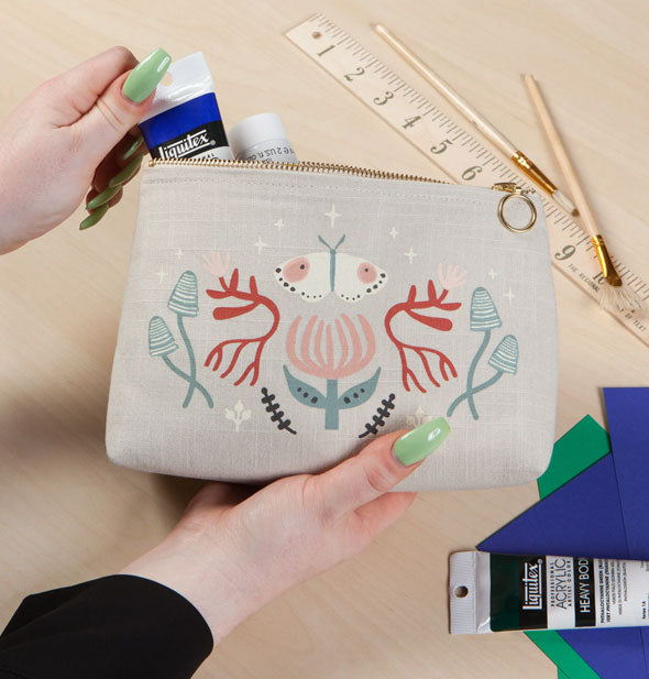Model removes a tube of paint from a Far and Away Small Cosmetic Bag