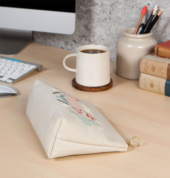 A Far and Away Small Cosmetic Bag lays on its side on a desktop to show its flat bottom and triangular shape