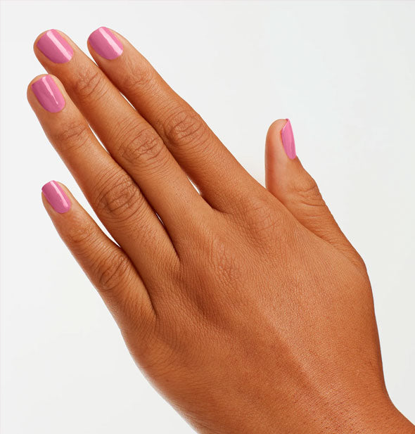 Model's hand wears a pink shade of nail polish