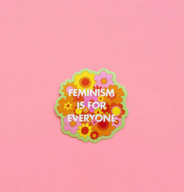 Sticker with vibrant pink, yellow, red, and orange floral design says, "Feminism is for everyone" in white lettering and features a green border