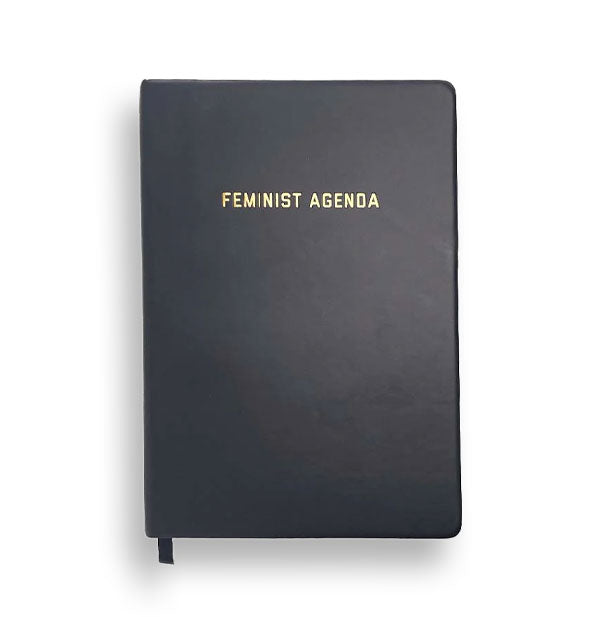 Black journal with ribbon bookmark extending from the bottom is stamped the words, "Feminist Agenda" in metallic gold foil