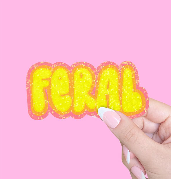 Model's hand holds a sticker that says, "Feral" in yellow bubble lettering with a sparkly orange border