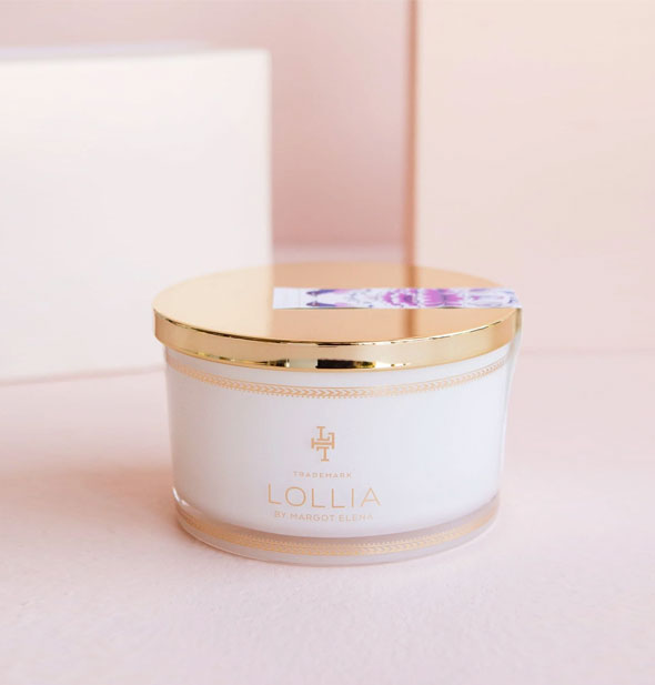 Whitish pot of Lollia bath salts with shiny gold lid secured by a purple floral sticker label