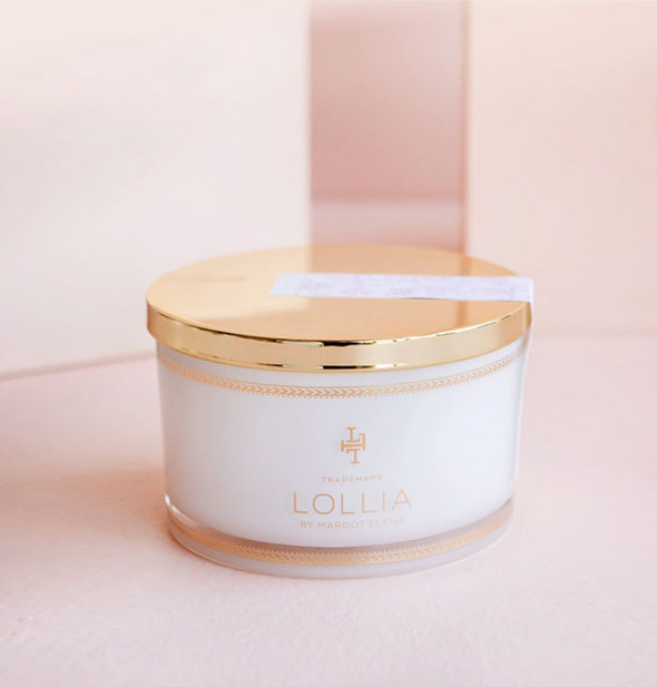 Whitish tub of Lollia bath salts with shiny gold lid secured by a floral sticker label