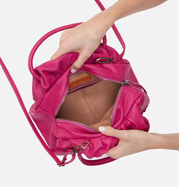 Model's hands hold open a dark pink leather satchel bag to reveal its tan interior