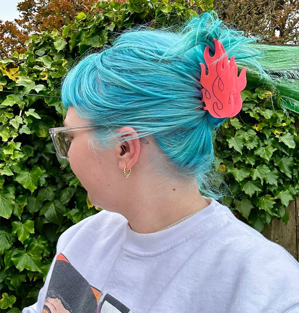 Model with blue hair wears a coral-colored flames claw clip in a swept-back style