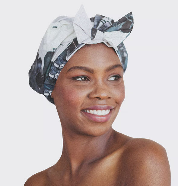 Smiling model wears a black and white floral print shower cap with bow in front