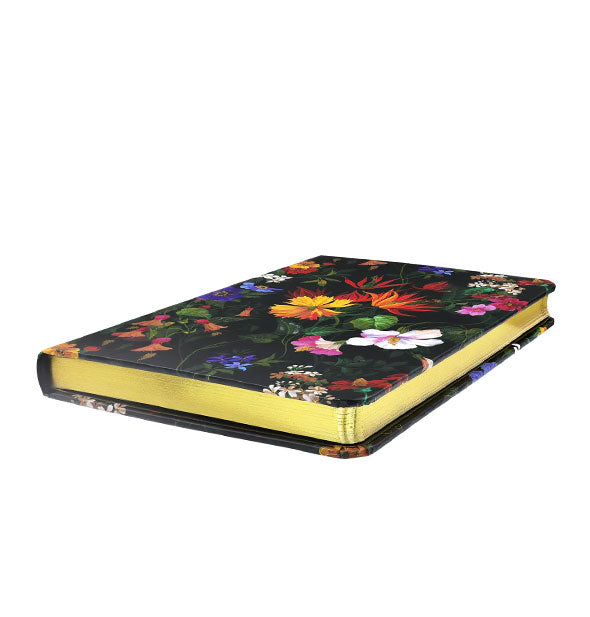 Three-quarter view of a black journal with colorful floral print reveals its gilded page edges