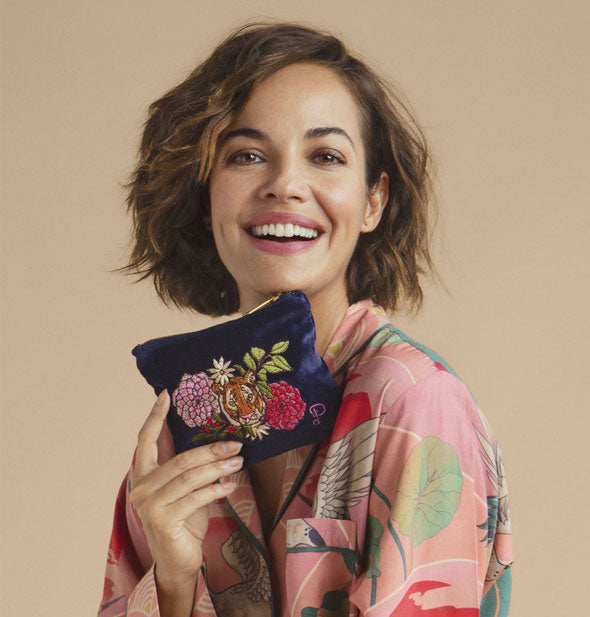 Smiling model holds a blue velvet floral tiger pouch under chin
