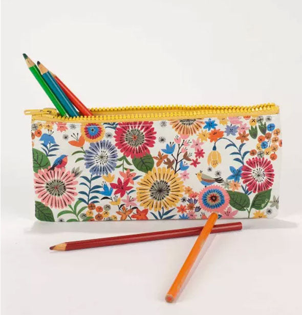 Unzipped flower pouch has several colored pencils sticking out of it and laying in front of it