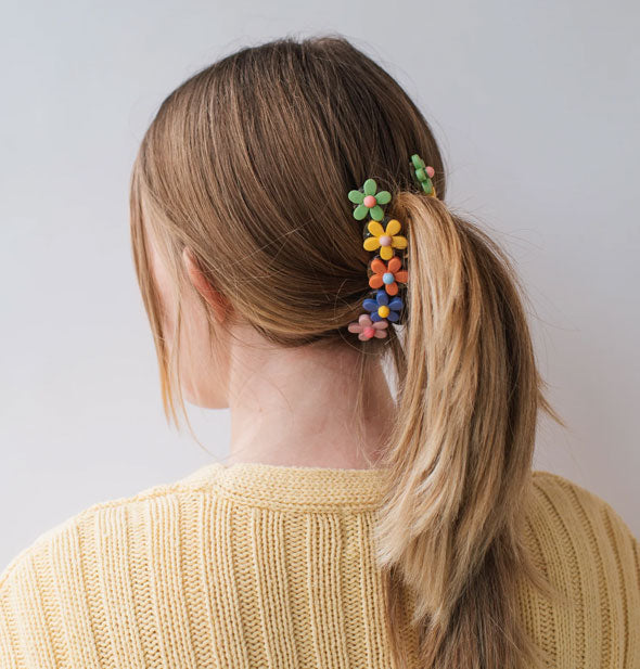 Model wears a colorful flower clip in a low-middle ponytail