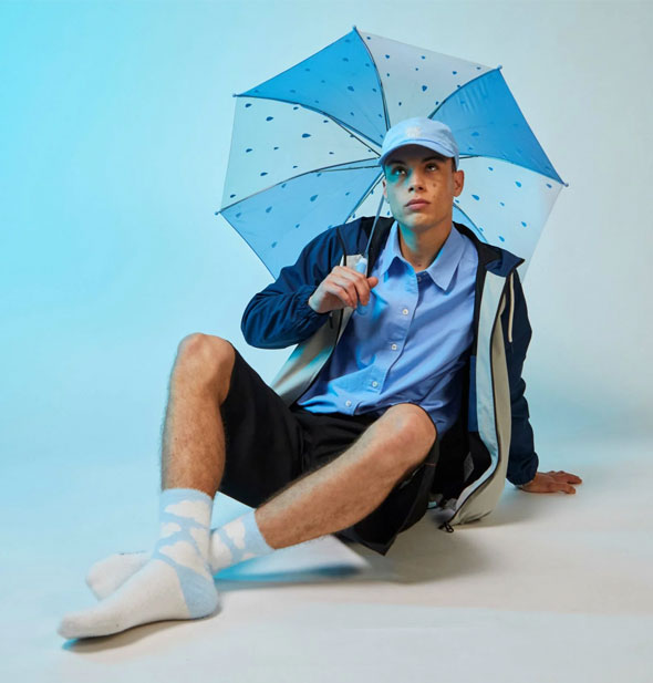 Sitting model holding a blue and white striped umbrella wears a pair of blue and white cloud print crew socks