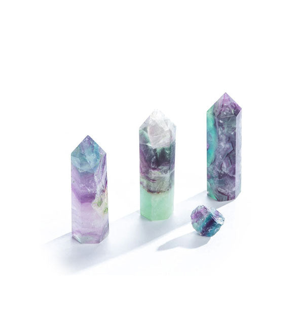 Three tall pointed fluorite crystals and one raw fluorite crystal piece, all in shades of purple and green