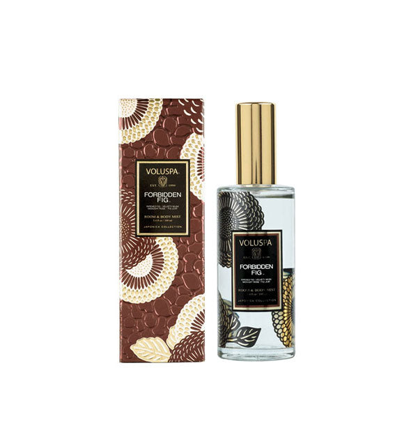 Black and gold floral-patterned clear glass bottle of Voluspa Forbidden Fig Room & Body Mist next to dark copper pebbled texture gift box with white and gold floral pattern