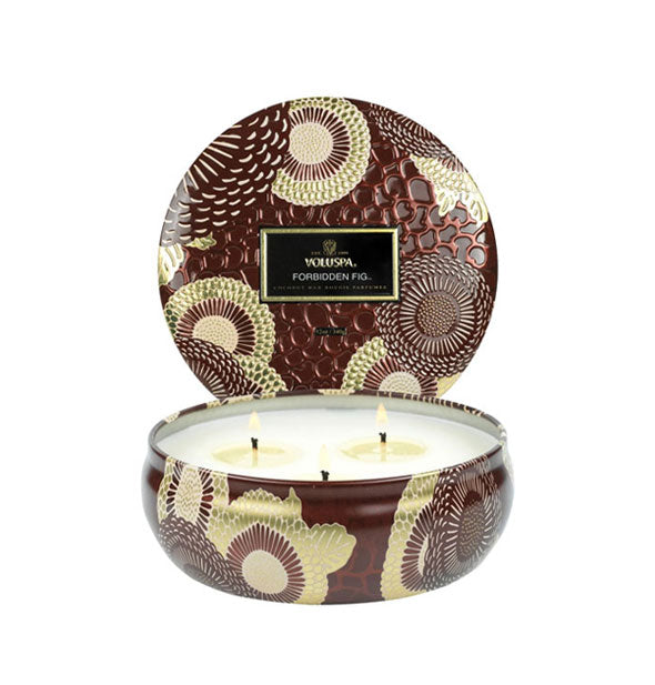 Decorative embossed tin Forbidden Fig Voluspa candle with three lit wicks