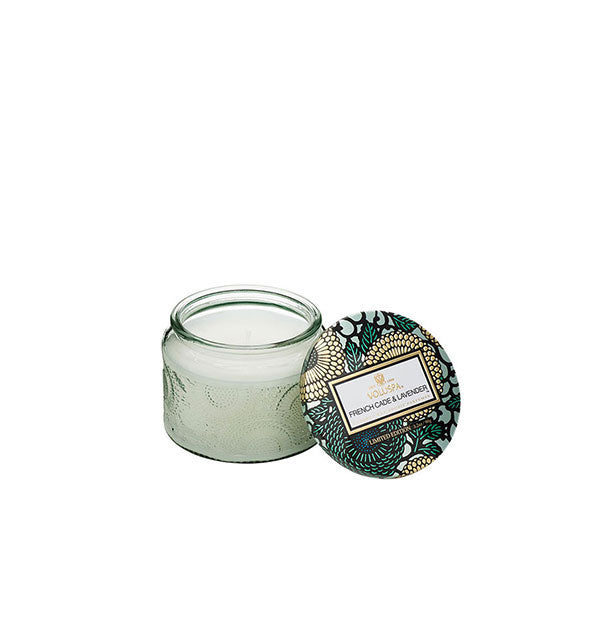 Light green embossed glass French Cade & Lavender Voluspa candle jar with green and gold metallic floral lid set to the side