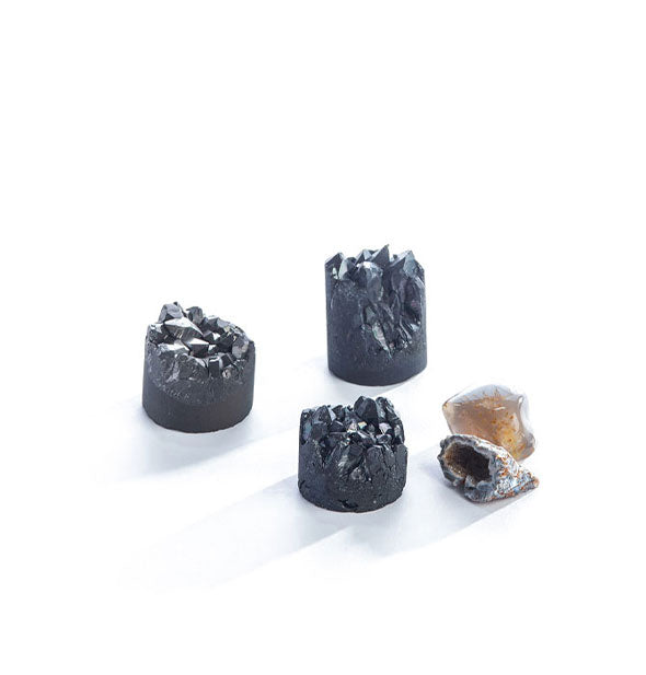 Three cylindrical black crystals and one rough lighter-colored crystal